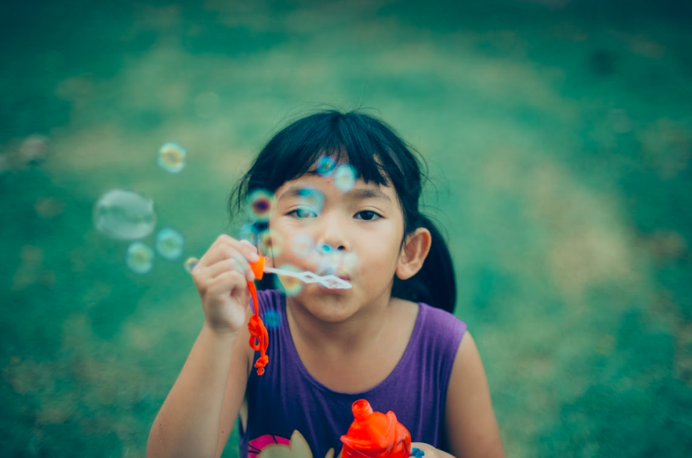 Young girl with bubbles at summer camp is happy she does not have lice because her parents followed summer lice prevention tips